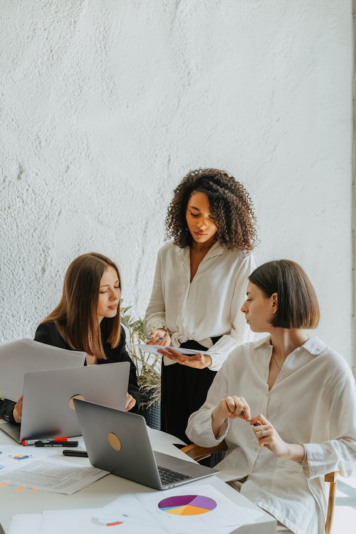 Home Three women collaborate on a project with charts and laptops in an office.